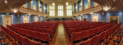 Breite Ansicht eines Konzertsaals mit roten Stühlen und Bühne