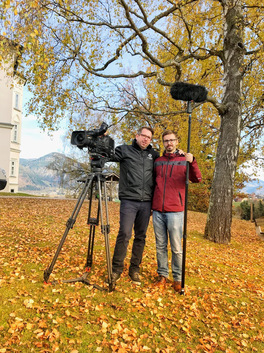 Videodreh mit Bernhard Raab vor einem Baum mit Kamera, Herbstlaub und Bergen im Hintergrund