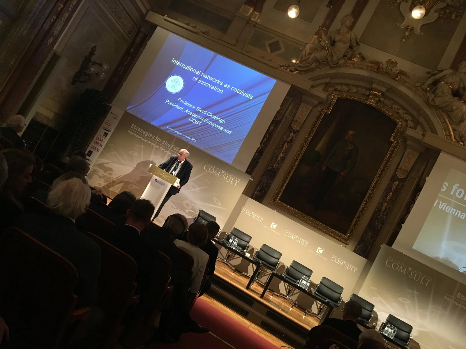 Mann spricht am Rednerpult, Bildschirm mit Text. Konferenz in einem großen Raum.